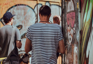Man in striped shirt facing colorful graffiti wall outdoors