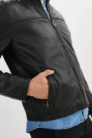 Man wearing black leather zip-up jacket with hand in pocket, blue shirt underneath