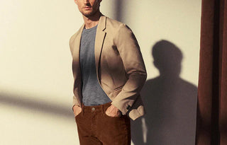 Man wearing beige blazer, blue t-shirt, and brown pants in natural light indoors
