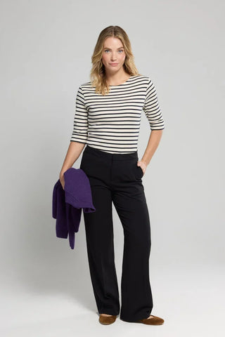 Woman in striped navy and white top with black wide-leg pants holding a purple sweater