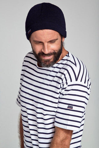 Man wearing a navy knit beanie and white striped Breton shirt, looking down and smiling