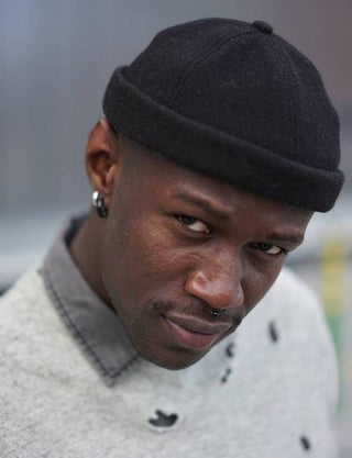 Man wearing a black wool beanie and light grey sweater with a serious expression
