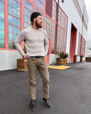 Man wearing a green wool beanie, beige sweater, khaki pants and black boots outdoors