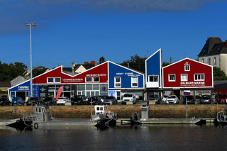 Colorful buildings with nautical signage and parked cars by a waterfront on a sunny day