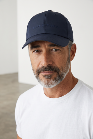A man wearing a navy blue Le Capitaine D'a Bord wool baseball cap with Loro Piana Rain System technology.