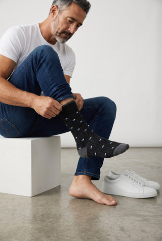 A man wearing Le Capitaine D'a Bord patterned cotton and cashmere socks in black with subtle blue details.