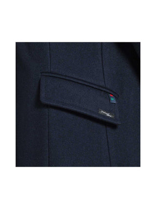 Close-up of navy wool coat pocket flap with small decorative tag and stitching detail.