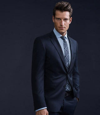 Man wearing navy wool suit and patterned tie against dark background