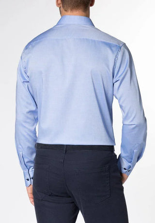 Man wearing a light blue long sleeve dress shirt and dark trousers, shown from the back