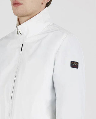 Man wearing a white nylon zip-up jacket with a patch on the sleeve, high collar style