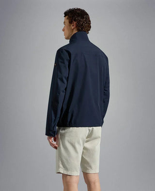Man wearing navy nylon jacket and light shorts, viewed from the back against a plain background