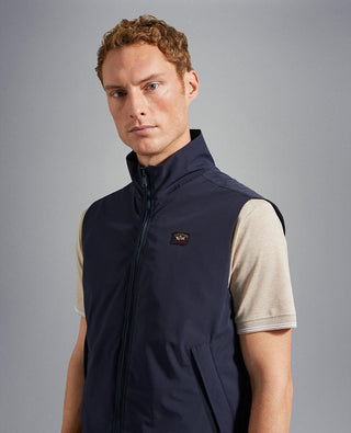 Man wearing a navy blue nylon sleeveless vest with zip front and chest logo patch